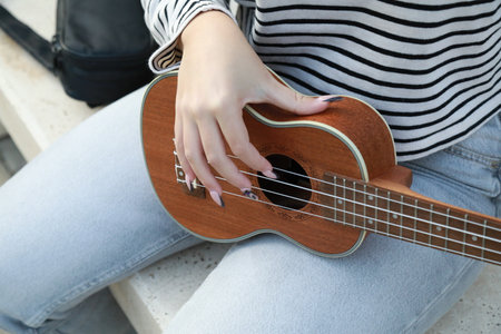 Young Woman Tunes The Ukulele Musical Instrument In A Park Outside