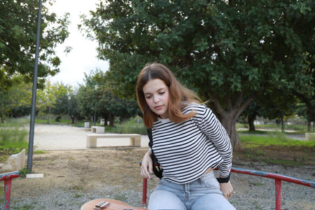 Girl Puts Backpack With Ukulele Musical Instrument On Shoulders And Walks In A Parkの写真素材