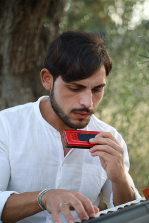 Boy Plays Music With Harmonica And Keyboard Among The Olive Trees