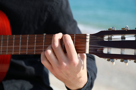 Hand Of A Man Plays Classical Guitar On The Beach Near The Sea In Summerの写真素材