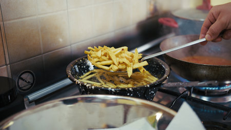 Chefs Hand Drains Spicy French Fries from Boiling Oil to Place in Paper Towelsの写真素材