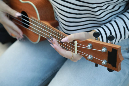 Young Woman Tunes The Ukulele Musical Instrument In A Park Outsideの写真素材