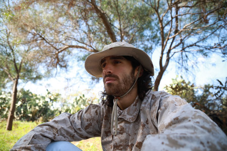 Sad Serviceman Sitting On The Ground In The Countryside Reflects On Memorial Dayの写真素材