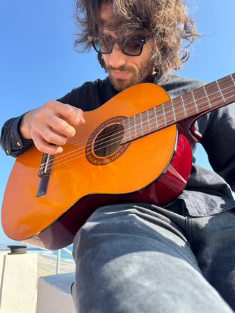 Long Hair Boy Plays Classical Guitar by the Ocean in Summer Dressed in Black