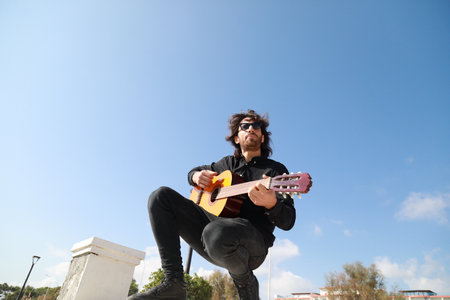 Young Long Hair Man Plays Guitar Outside, Low Angle