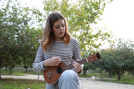 Girl Strums With Ukulele Musical Instrument Near A Tree