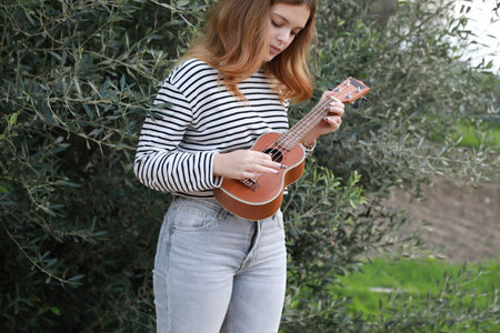Girl Strums With Ukulele Musical Instrument Near A Tree