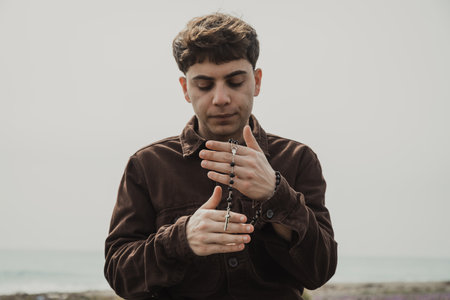 Christian Man Praying With A Rosary And Eyes Closed On The Shore