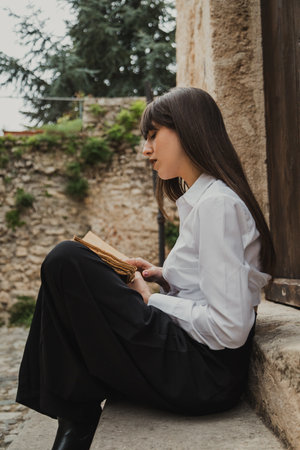 Young Woman Reading An Ancient Book With Passion Sitting On A Building Steps