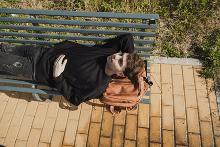 Tired Man Sleeping On His Backpack While On A Bench Outdoorの写真素材