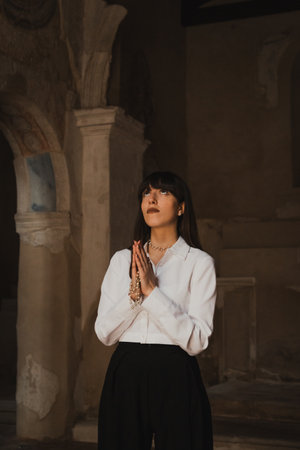 Woman Standing Still In The Middle Of An Old Church And Prayingの写真素材