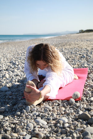 Fit Blonde Woman Doing Leg Stretches on Sandy Beachの写真素材