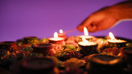 Silhouette of hand lighting candles amidst flowers for Diwaliの写真素材