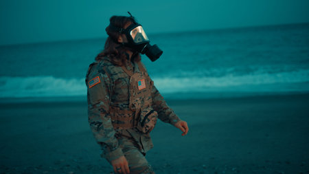 American Soldier With Gas Mask Walks on Shoreline Near Stormy Ocean at Night