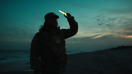 American soldier lights a chemical light at night near the ocean at sunsetの写真素材