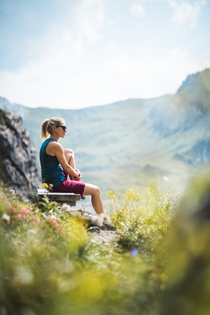 Beautiful Sportive Hiker girl having a break and relaxing on a bench near a lake enjoying the sunshineの写真素材