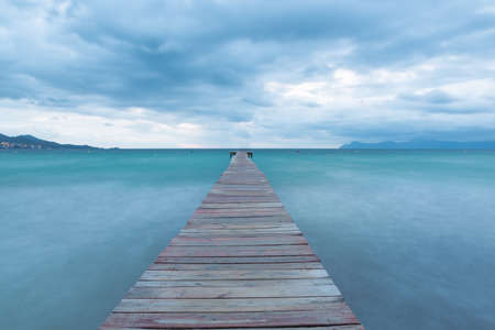 Dramatic Looking Morning at the Sea in Spain - Majorca. Blue Hour with Clouds on the Wooden Pier / Jetty の写真素材