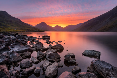 Colourful Orange And Red Sky At Sunrise With Rocks On The Lake Shoreline. Lake District, UK.の写真素材