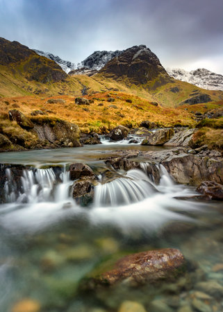 Small Cascading Waterfall Stream At Deepdale Beck In The Lake District National Park With Snow On Mountain Peaks.の写真素材