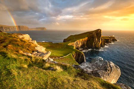 Iconic Isle of Skye lighthouse at Neist Point with beautiful golden light and rainbow over coast.の写真素材
