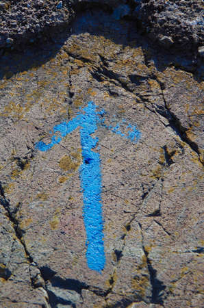Blue arrow painted on a lichen covered rock at the seashore.の写真素材