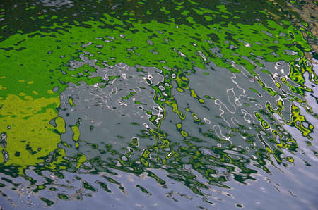 Bright green, blue and grey pattern of a boathouse reflected in the ripples of the sea.の写真素材
