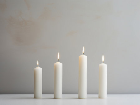 Four white candles on a white table against the background of a beige wallの素材