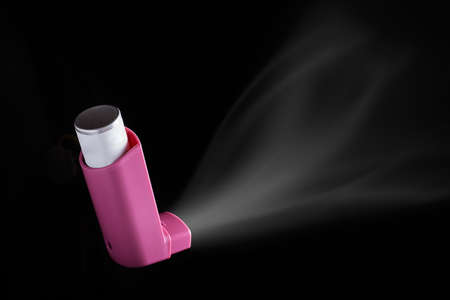 MDI Inhaler being pushed over black background. Asthma aerosol for people with respiratory problemsの写真素材