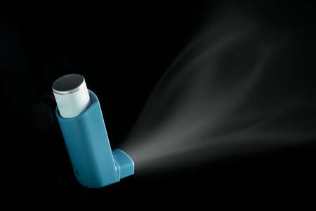 MDI Inhaler being pushed over black background. Asthma aerosol for people with respiratory problemsの写真素材