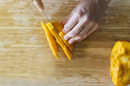 Woman cutting mango on a wooden board to prepare a healthy salad seen from a zenithal planeの写真素材