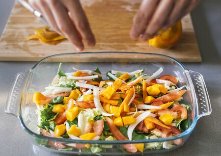 Woman putting mango in a huge saladの写真素材