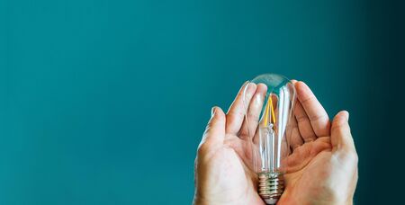 Two hands holding a light bulb on a green background with copy spaceの写真素材