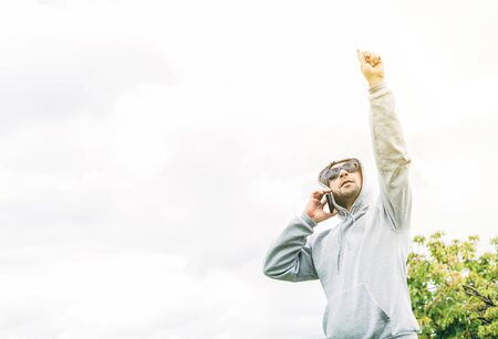 A young A young man with blue sunglasses, gray sweatshirt and beard talking on a cell phone looking upの写真素材