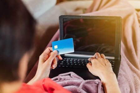 Woman lying on the sofa and shopping online from home with her tablet and credit cardの写真素材