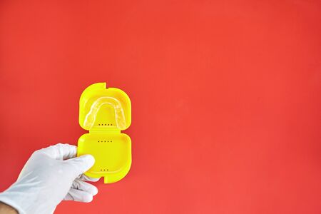 Invisible braces in a yellow case on a red background held in one hand by a latex gloveの写真素材