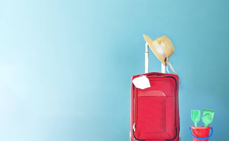 Red suitcase with straw hat, Coronavirus mask on green background and children's bucket with rake and shovelの写真素材