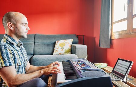 Man playing piano while taking online lessons at home.の写真素材