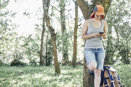 Woman resting on a tree and consulting her mobile phone during a day of walking