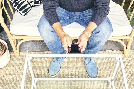 Man in jeans sitting on a couch consulting the phoneの写真素材