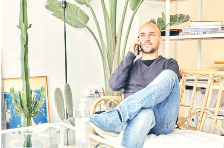 Caucasian man in jeans sitting on a couch talking on the phoneの写真素材