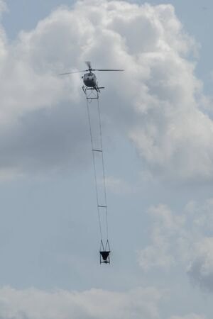 helicpter flying with big barrel of lime over a forestの写真素材