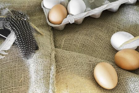 different coloured eggs with feathers lying on a jute bagの写真素材