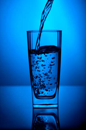 Serving water in a glass reflected on the ground on a blue backgroundの写真素材