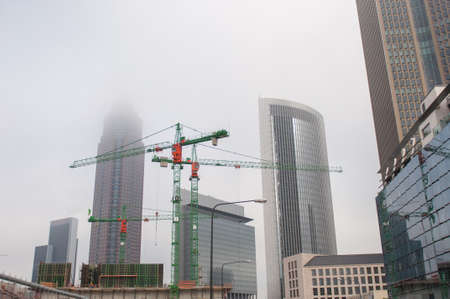 Construction cranes in the middle of the city of Frankfurt surrounded by fogの写真素材
