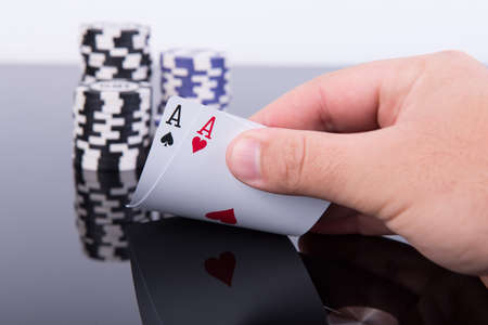 Hand holding a pair of aces with a stack of chips behind on black reflective table