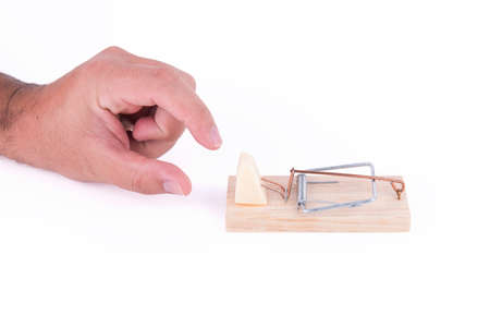 Hand trying to catch a piece of cheese on a mousetrap on white backgroundの写真素材