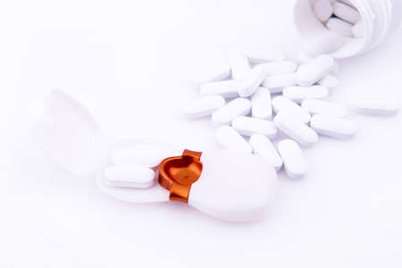 Bottle of spilled pills on a white table next to a pillbox