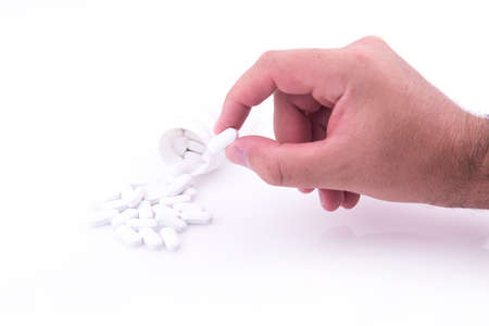 Bottle of spilled pills on a white table and a hand picking up a pill