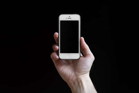 Man holding smartphone with empty screen isolated on black background. Male hands with phone, space...