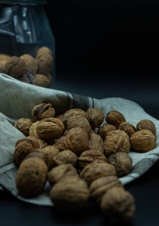 nuts on kitchen cloth, in the back a jar full of nuts, on a black background, healthy food concept.